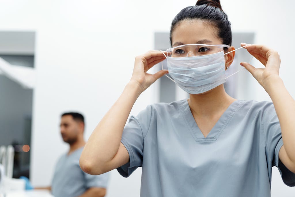 Asian female graduate nurse adjusts protective mask and goggles in a medical setting.