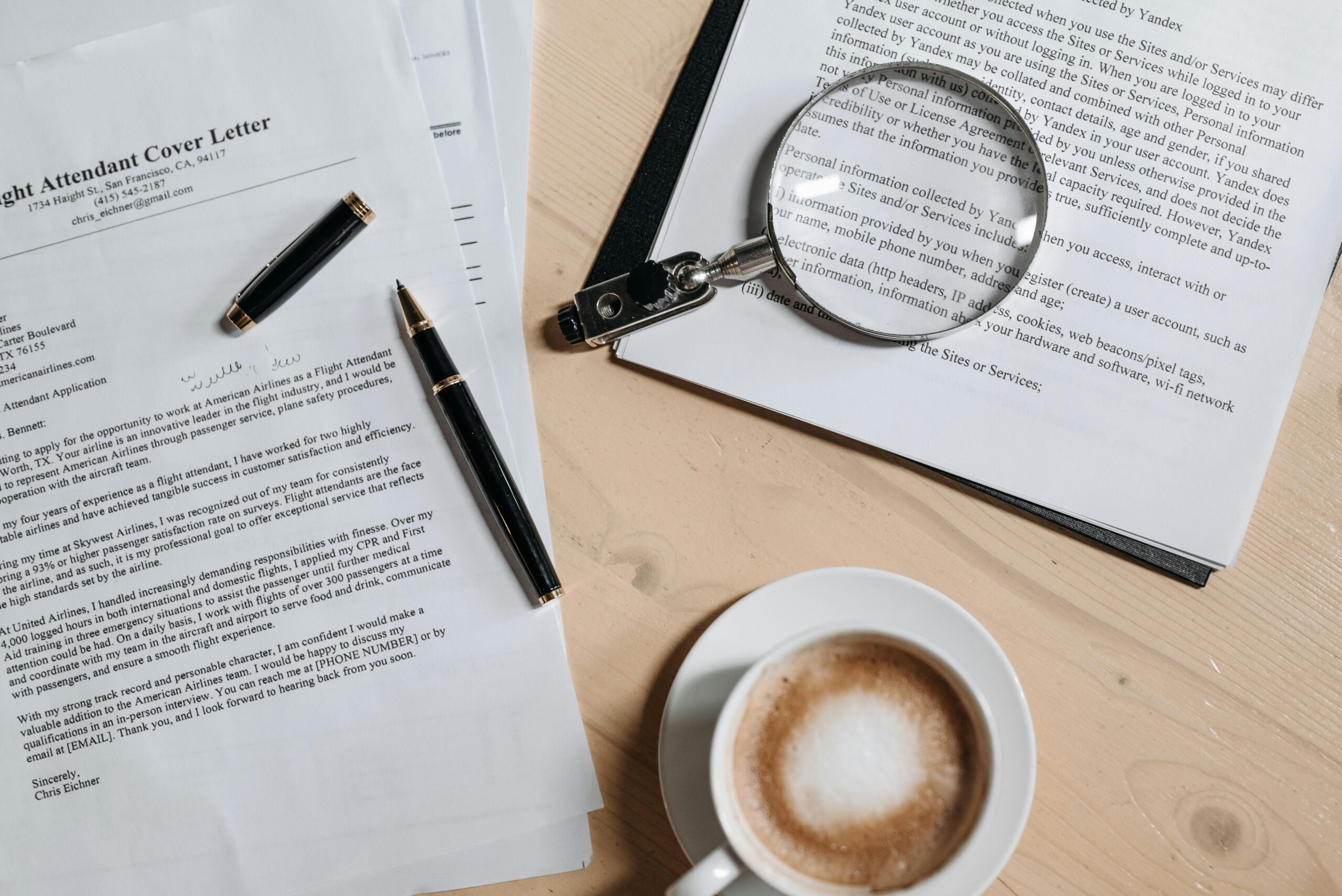 A top view of coffee and job application and cover letter for a career change and documents with a magnifying glass on a wooden desk.