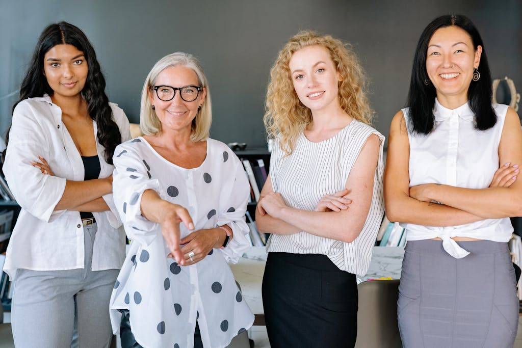 Smiling diverse group of businesswomen who did a career change at 40, arms crossed, in modern office setting.