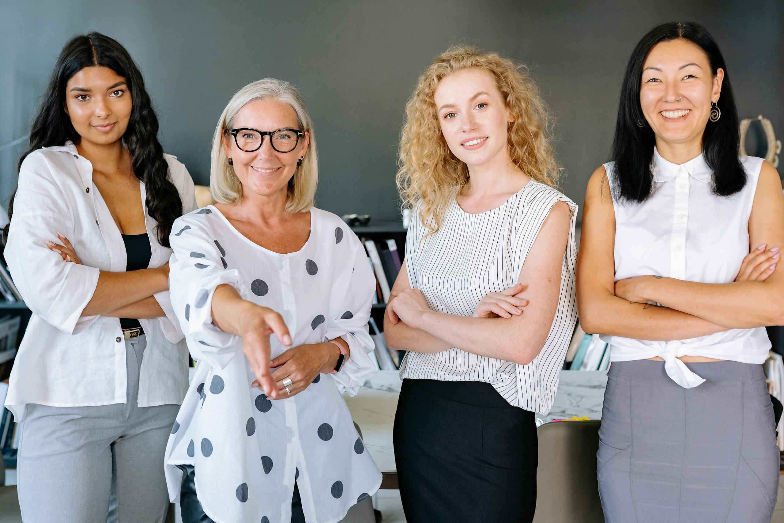 Smiling diverse group of businesswomen who did a career change at 40, arms crossed, in modern office setting.
